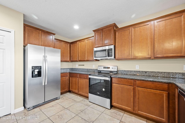 kitchen with dark stone countertops, appliances with stainless steel finishes, light tile patterned floors, and a textured ceiling