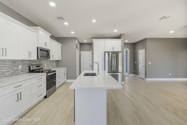 kitchen with sink, backsplash, stainless steel appliances, an island with sink, and white cabinets