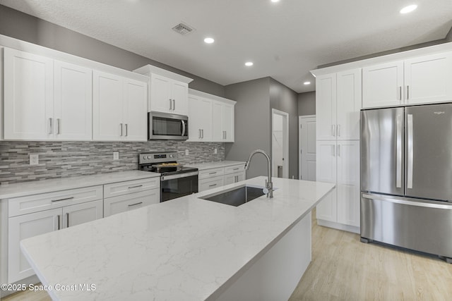 kitchen featuring sink, light hardwood / wood-style flooring, appliances with stainless steel finishes, white cabinetry, and light stone countertops