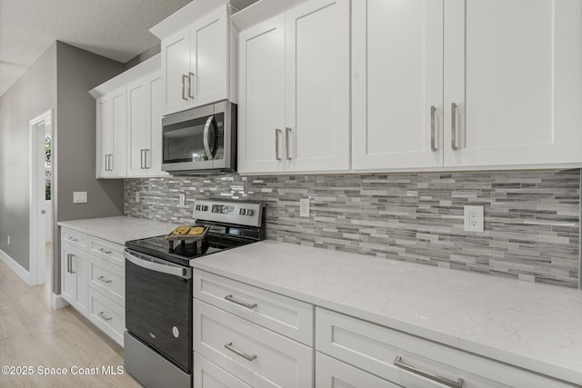 kitchen featuring appliances with stainless steel finishes, tasteful backsplash, white cabinets, light stone countertops, and light hardwood / wood-style flooring