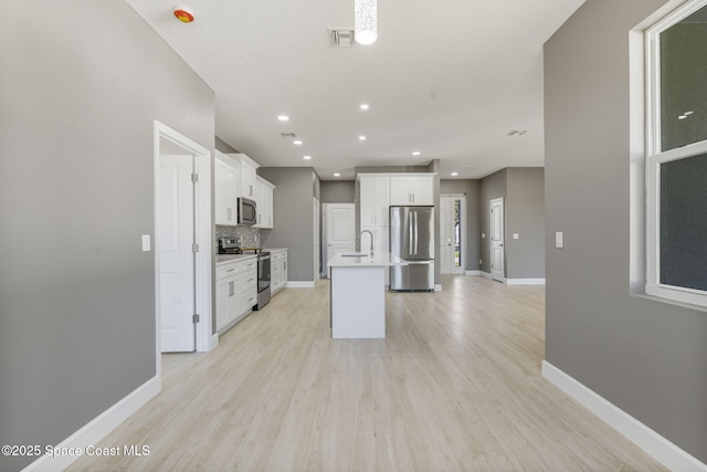 kitchen with sink, a kitchen island with sink, white cabinetry, backsplash, and stainless steel appliances