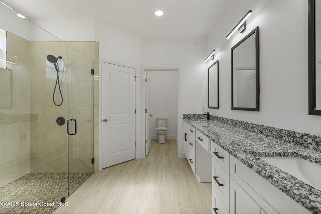 bathroom with a shower with door, wood-type flooring, vanity, and toilet