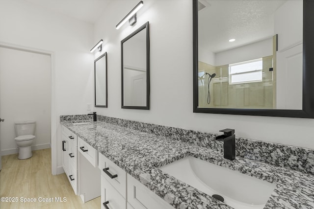 bathroom featuring hardwood / wood-style flooring, vanity, walk in shower, toilet, and a textured ceiling