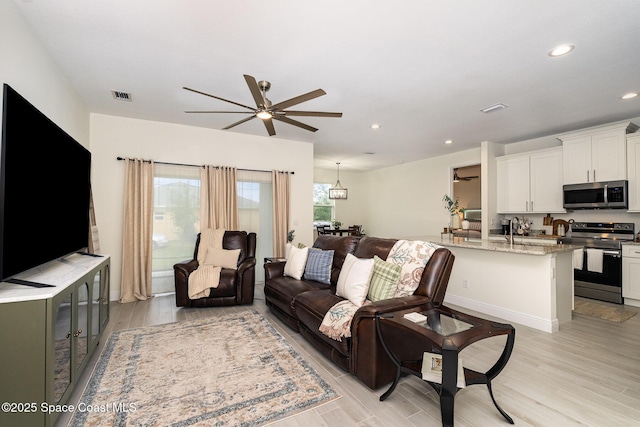 living room with ceiling fan, sink, and light wood-type flooring