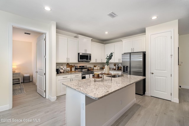 kitchen featuring sink, light stone counters, a center island with sink, appliances with stainless steel finishes, and white cabinets