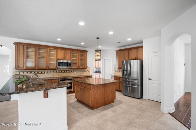 kitchen with a kitchen bar, sink, hanging light fixtures, dark stone countertops, and stainless steel appliances