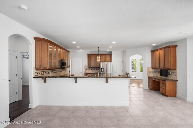 kitchen featuring appliances with stainless steel finishes, a kitchen breakfast bar, tasteful backsplash, decorative light fixtures, and dark stone counters