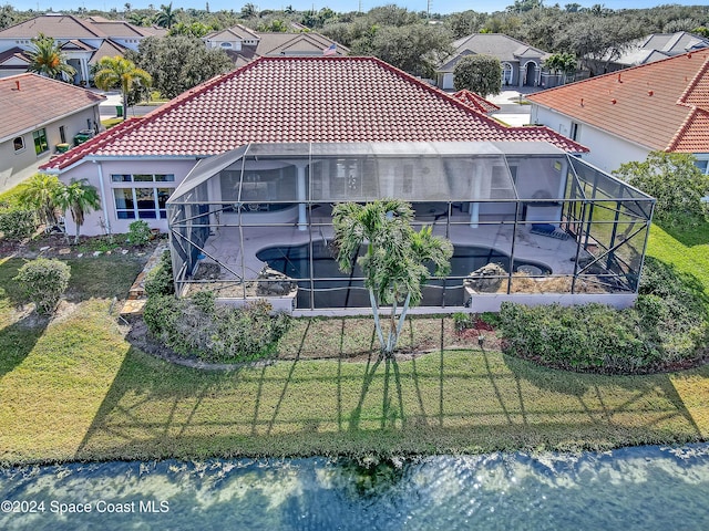 back of house with a water view, a pool with hot tub, glass enclosure, and a lawn