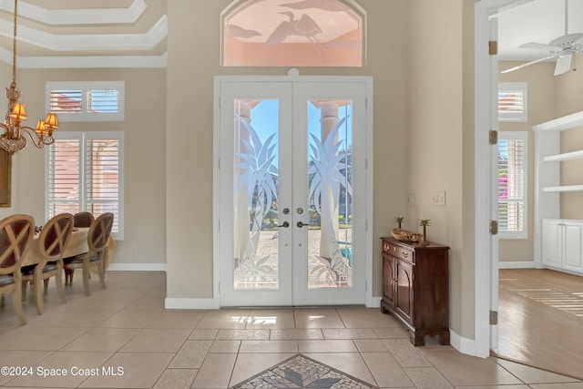 tiled entryway featuring french doors, crown molding, a chandelier, and a high ceiling