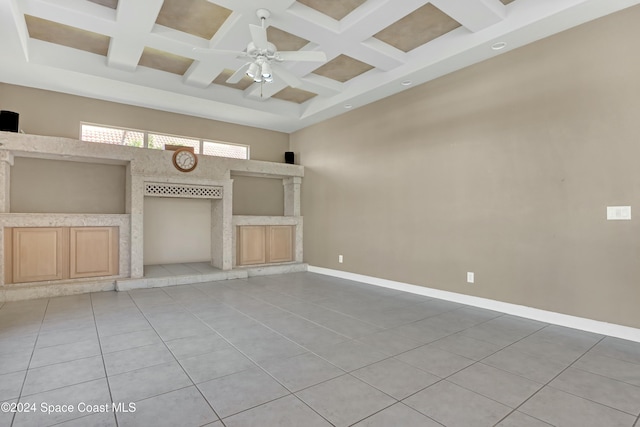 unfurnished living room with ceiling fan, a high ceiling, coffered ceiling, light tile patterned flooring, and beamed ceiling