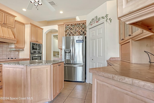 kitchen with light tile patterned flooring, light brown cabinets, appliances with stainless steel finishes, ceiling fan, and decorative backsplash