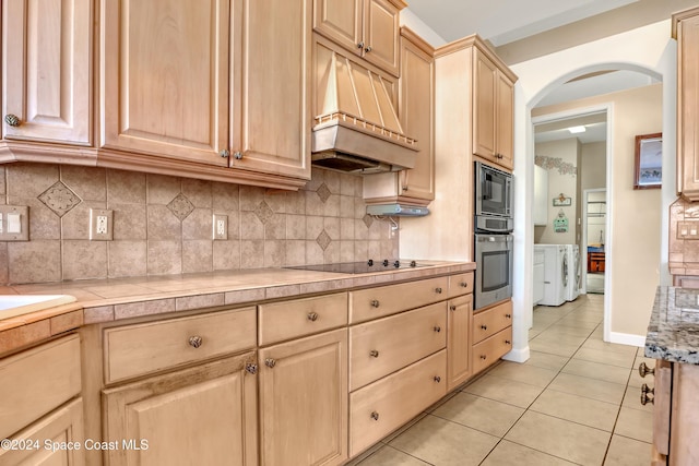 kitchen with premium range hood, independent washer and dryer, black electric stovetop, built in microwave, and stainless steel oven