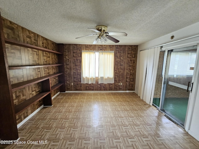 unfurnished room with ceiling fan, plenty of natural light, wooden walls, and a textured ceiling