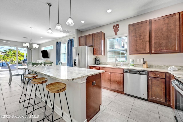 kitchen with appliances with stainless steel finishes, decorative light fixtures, a center island, and sink