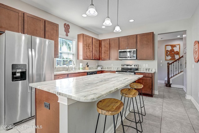 kitchen featuring sink, light stone counters, hanging light fixtures, appliances with stainless steel finishes, and a kitchen island