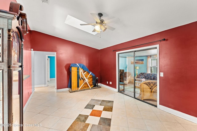 tiled empty room featuring vaulted ceiling with skylight and ceiling fan