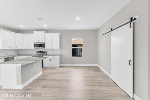 kitchen featuring white cabinetry, light stone countertops, light hardwood / wood-style floors, stainless steel appliances, and a barn door