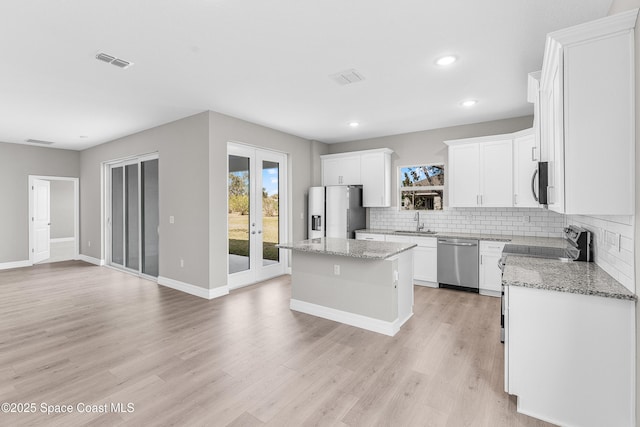 kitchen featuring sink, appliances with stainless steel finishes, white cabinetry, a center island, and light stone counters