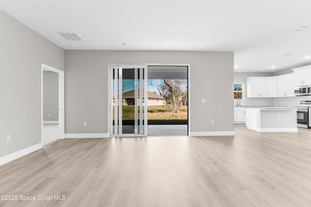 unfurnished living room featuring plenty of natural light, sink, and light hardwood / wood-style flooring