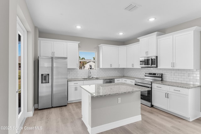 kitchen with a kitchen island, appliances with stainless steel finishes, sink, white cabinets, and light stone countertops