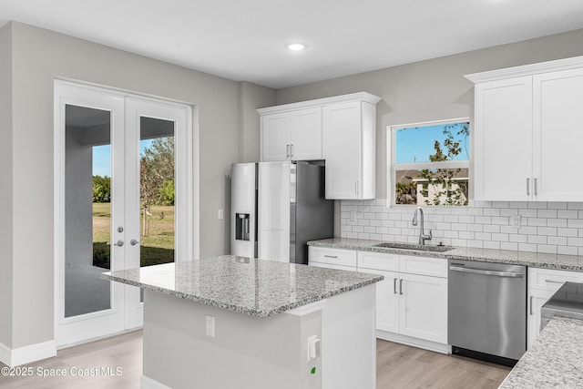 kitchen with sink, light stone counters, appliances with stainless steel finishes, a kitchen island, and white cabinets