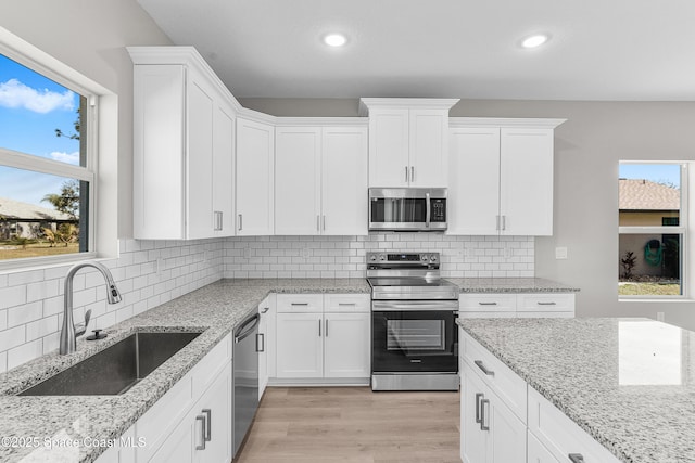 kitchen with sink, white cabinetry, stainless steel appliances, light stone countertops, and light wood-type flooring