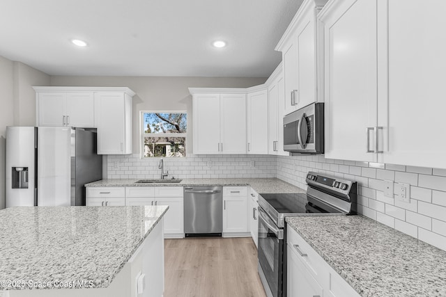 kitchen with sink, light wood-type flooring, appliances with stainless steel finishes, light stone countertops, and white cabinets