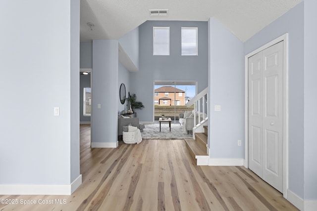 hallway with a high ceiling, a textured ceiling, and light wood-type flooring