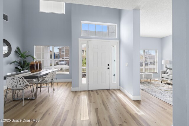 entryway with a towering ceiling, light hardwood / wood-style floors, and a textured ceiling