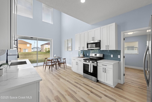 kitchen featuring sink, light hardwood / wood-style flooring, white cabinetry, stainless steel appliances, and decorative backsplash