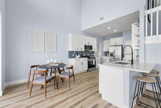 kitchen featuring sink, a breakfast bar, appliances with stainless steel finishes, white cabinetry, and decorative backsplash