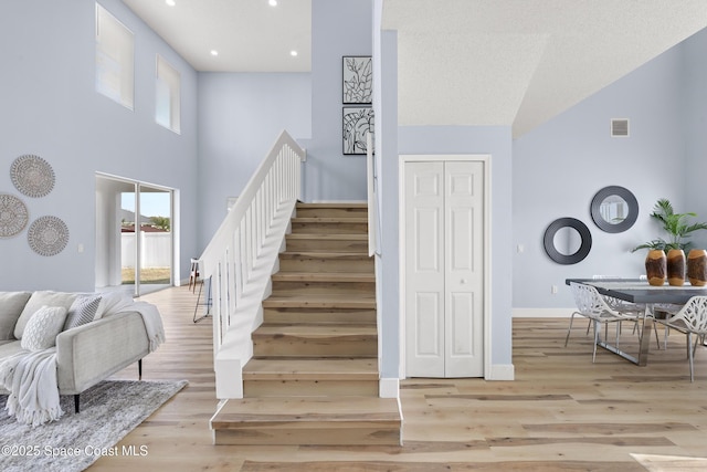 stairs featuring a towering ceiling and wood-type flooring