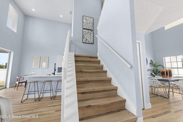 stairway with a towering ceiling, sink, and hardwood / wood-style floors