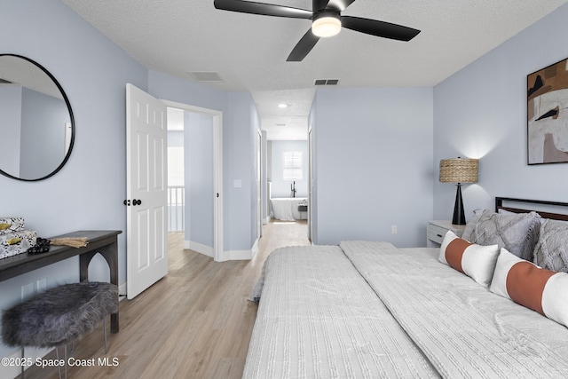 bedroom with ceiling fan, ensuite bath, a textured ceiling, and light wood-type flooring