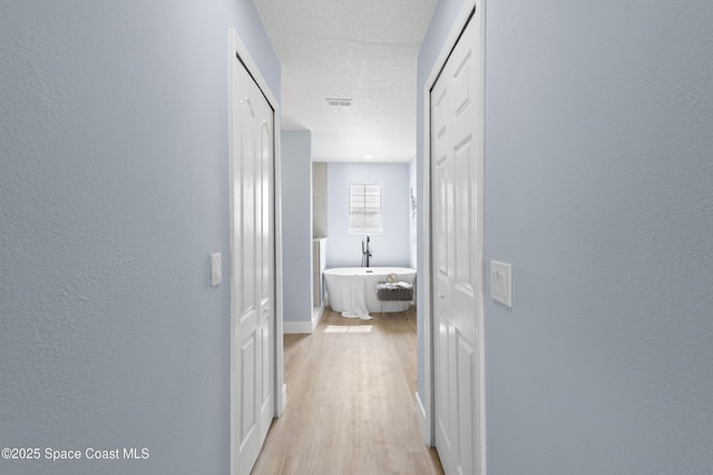 hall featuring light hardwood / wood-style flooring and a textured ceiling