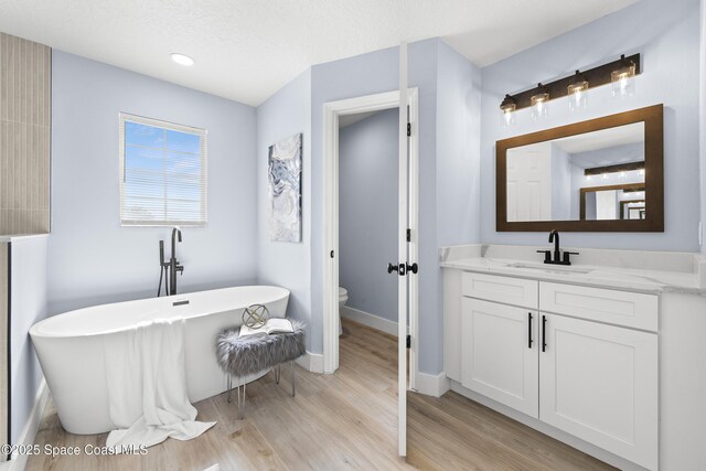 bathroom with vanity, a bath, hardwood / wood-style floors, and toilet