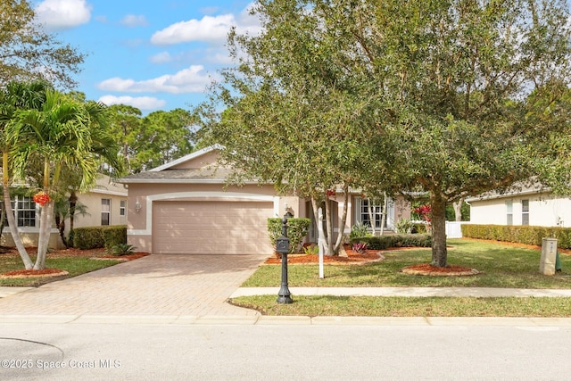 view of front facade featuring decorative driveway, a front yard, an attached garage, and stucco siding