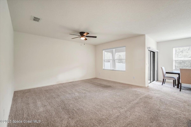 carpeted empty room with ceiling fan, plenty of natural light, and a textured ceiling