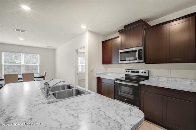 kitchen featuring sink, dark brown cabinets, stainless steel appliances, an island with sink, and a healthy amount of sunlight