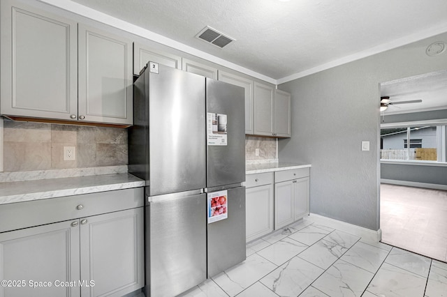 kitchen with gray cabinetry, a textured ceiling, stainless steel refrigerator, ceiling fan, and decorative backsplash