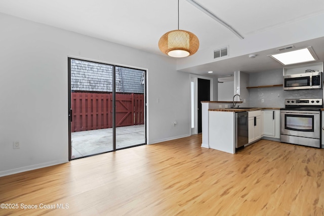 kitchen with white cabinetry, light hardwood / wood-style flooring, appliances with stainless steel finishes, kitchen peninsula, and pendant lighting