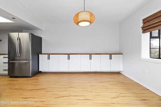 kitchen featuring stainless steel fridge, decorative light fixtures, light hardwood / wood-style flooring, and white cabinets