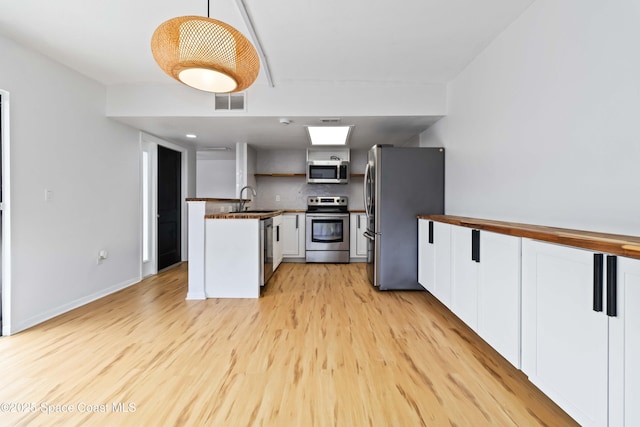 kitchen featuring white cabinetry, stainless steel appliances, light hardwood / wood-style floors, decorative backsplash, and decorative light fixtures