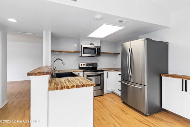 kitchen featuring sink, butcher block counters, stainless steel appliances, light hardwood / wood-style floors, and white cabinets