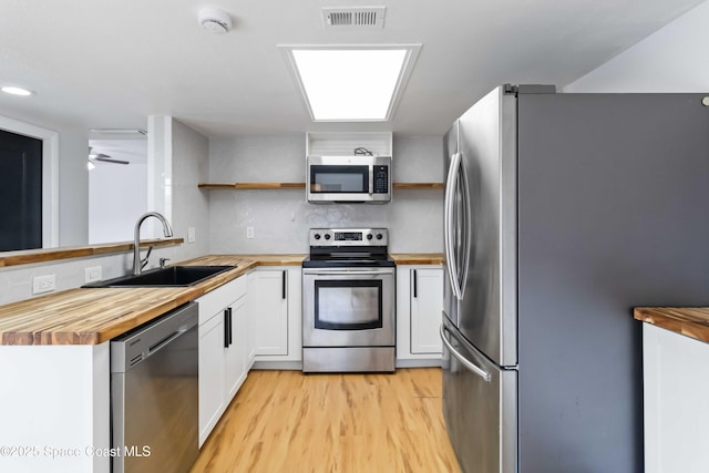 kitchen with sink, wooden counters, light hardwood / wood-style flooring, appliances with stainless steel finishes, and white cabinets