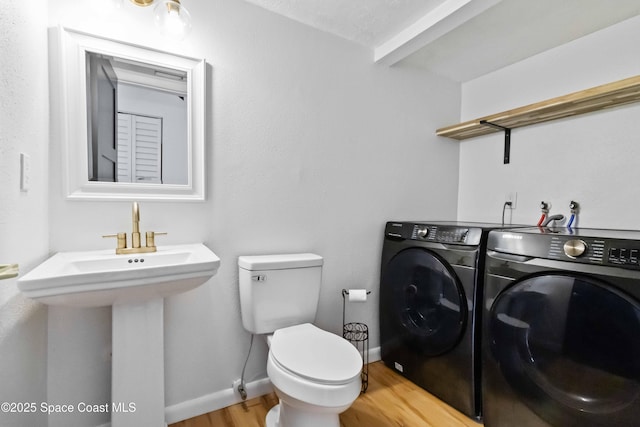 bathroom with washing machine and clothes dryer, wood-type flooring, toilet, and sink