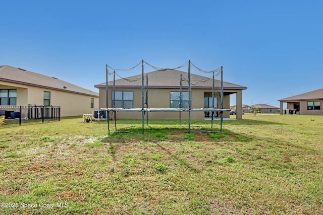 rear view of property with a trampoline and a lawn