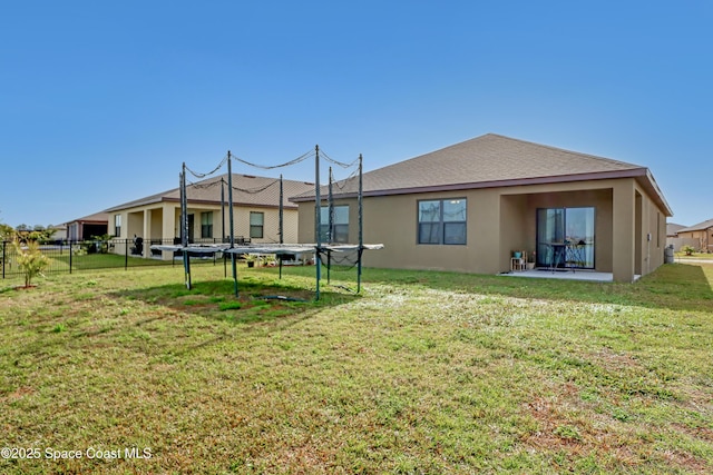 back of house with a patio area, a trampoline, and a lawn