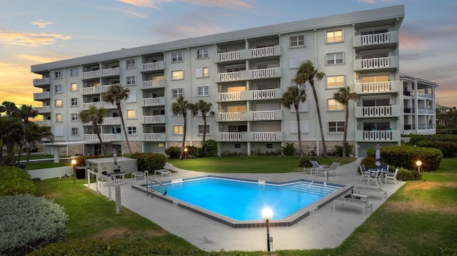 pool at dusk featuring a patio and a yard