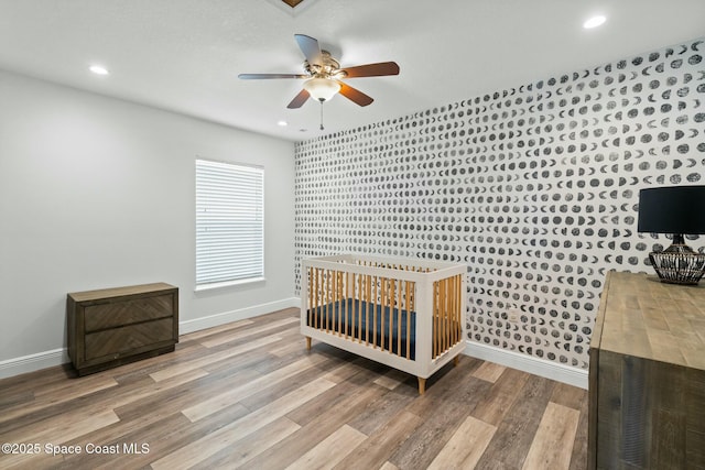 bedroom with a crib, wood-type flooring, and ceiling fan